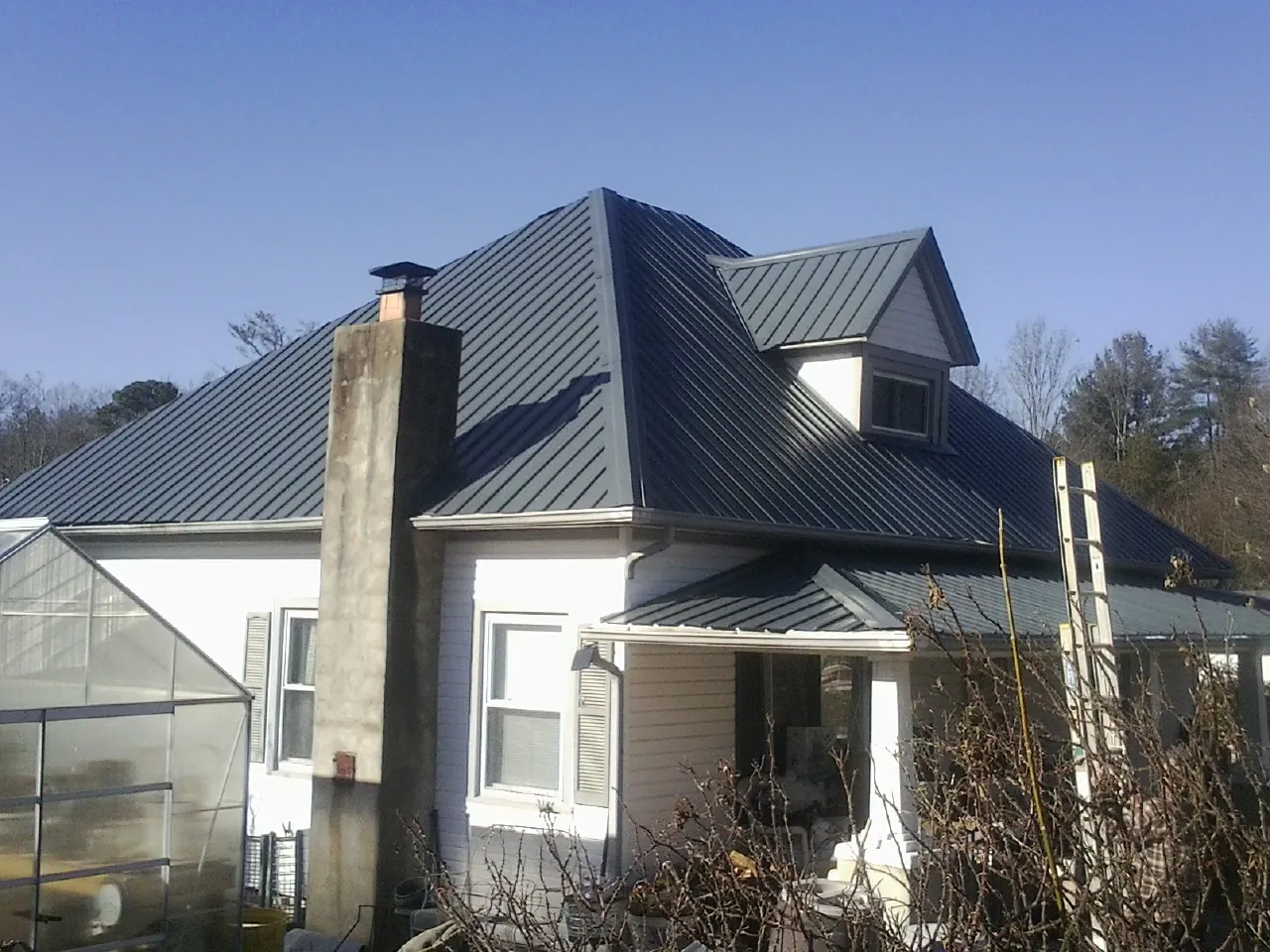 Dark blue standing seam metal roof on a white farmhouse with dormer — Slate & Tile Roof Repair by Roofing Brothers in Concrete