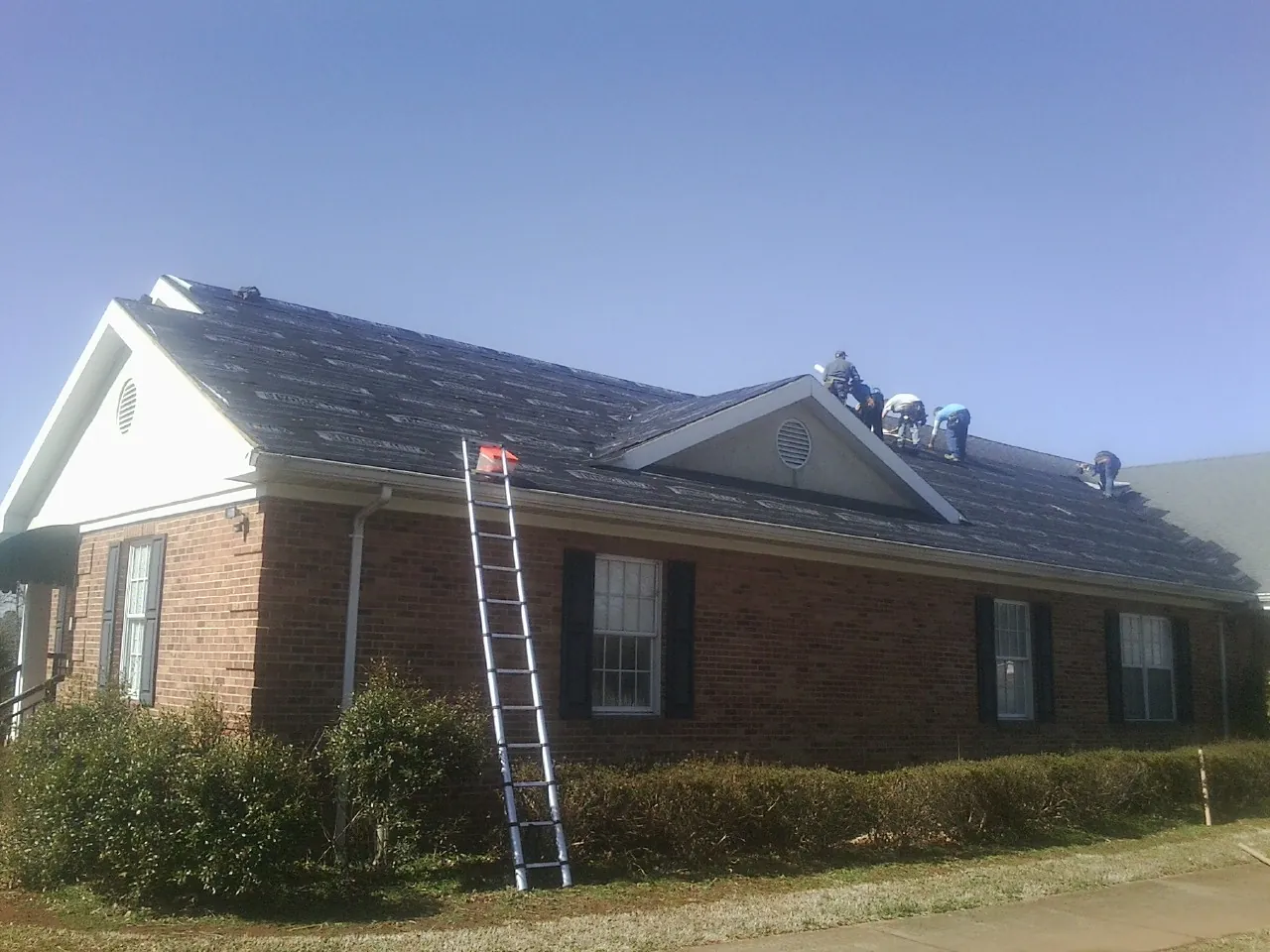 Crew tearing shingles off a brick ranch roof with a ladder set — Metal Roof Repair work by our crew in Concrete