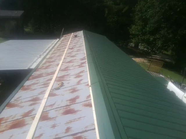 Old rusted panels beside newly installed green metal roofing — Wind Damage Roof Repair by Roofing Brothers in Concrete