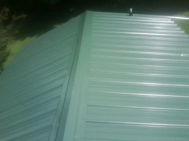 New green metal panels meeting at the ridge of a roof — Flat Roof Repair work by our crew in Concrete