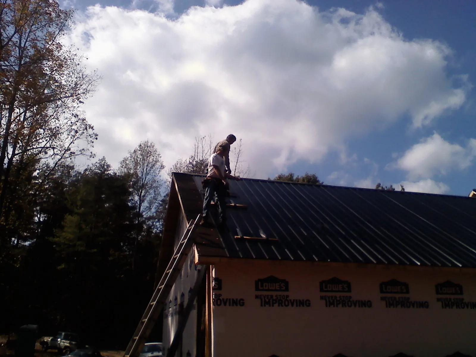 Roofer fastening dark metal panels high against a cloudy sky, from a Roof Inspection job in Concrete