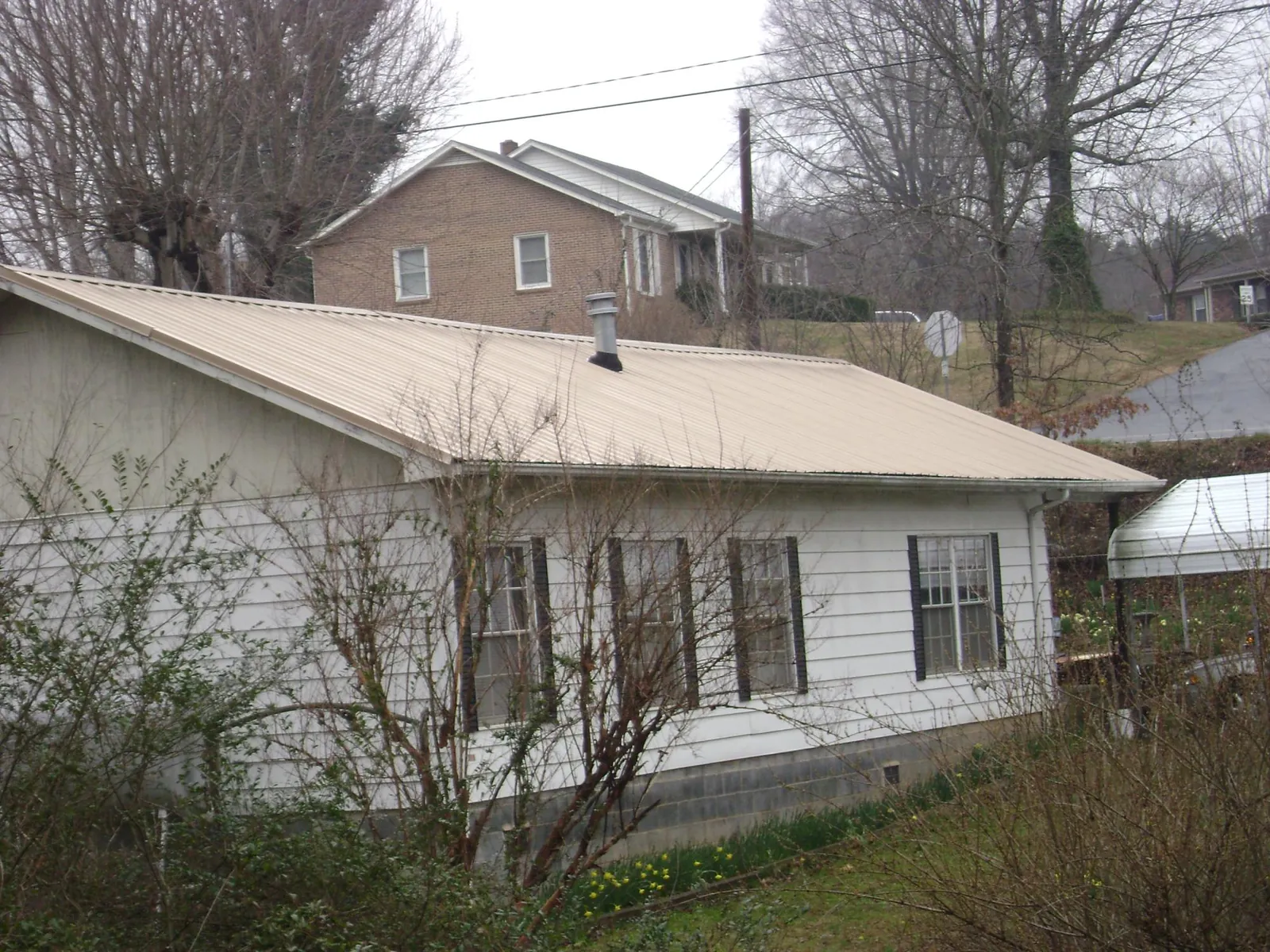 Tan metal roof on a white sided house set into a hillside — Commercial Roofing by Roofing Brothers in Concrete